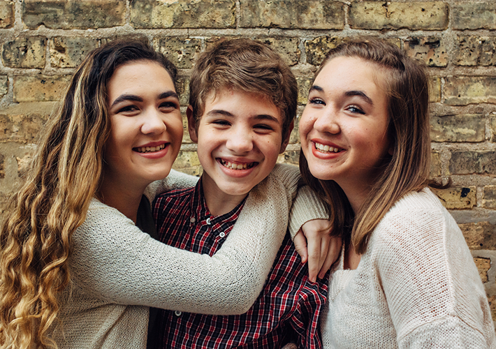 Two sisters and a brother smiling in front of a brick wall
